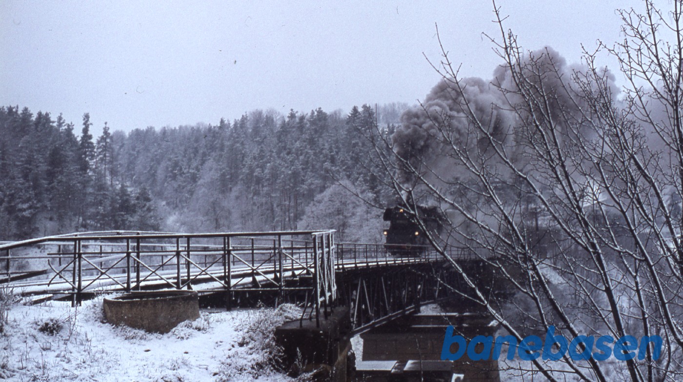 Persontog med damplokomotiv i snevejr på vej over sneklædt bro Persontog med damplokomotiv i snevejr på vej over sneklædt bro