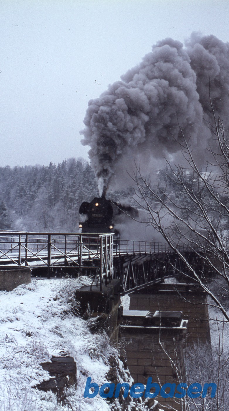 Persontog med damplokomotiv i snevejr på vej over sneklædt bro Persontog med damplokomotiv i snevejr på vej over sneklædt bro