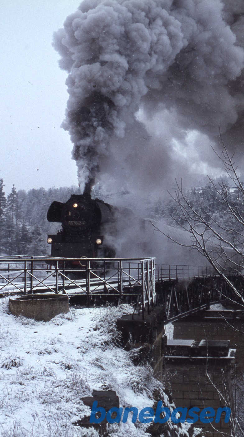 Persontog med damplokomotiv i snevejr på vej over sneklædt bro Persontog med damplokomotiv i snevejr på vej over sneklædt bro