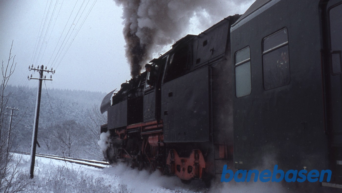 Persontog med damplokomotiv i snevejr på vej over sneklædt bro Persontog med damplokomotiv i snevejr på vej over sneklædt bro