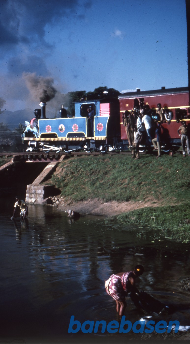 Et overfyldt damptog krydser en lille å, hvor kvinderne vasker tøj Et overfyldt damptog krydser en lille å, hvor kvinderne vasker tøj