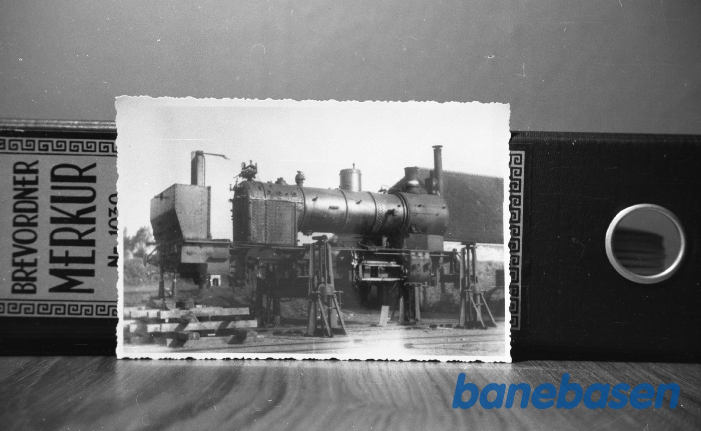 Det "afklædte" lokomotiv er et af Gudhjembanens to lokomotiver, som renoveres på Gudhjem station, formentlig i 1928. På daværende tidspunkt lå Nexø-banen endnu med det oprindelige spor, som var for spinkelt til at kunne bære disse lokomotiver Det "afklædte" lokomotiv er et af Gudhjembanens to lokomotiver, som renoveres på Gudhjem station, formentlig i 1928. På daværende tidspunkt lå Nexø-banen endnu med det oprindelige spor, som var for spinkelt til at kunne bære disse lokomotiver