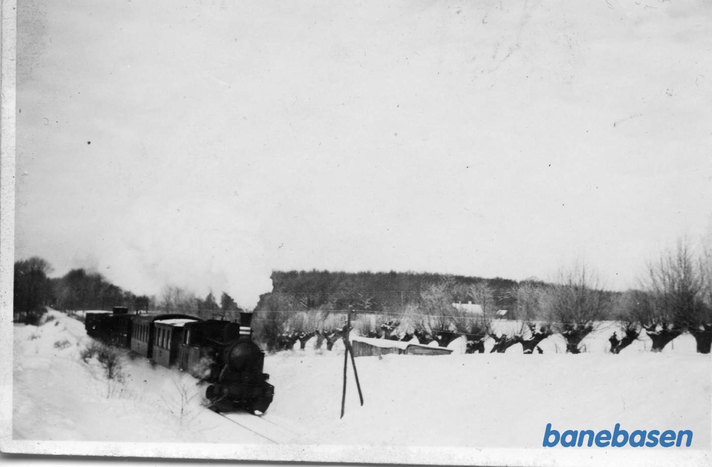 Præstøbanetoget er på vej mod Præstø. I baggrunden ses Oregårdsvængeskoven og her på dæmningen ligger Faksinge sø til venstre (ses ej)  Faksinge trinbræt