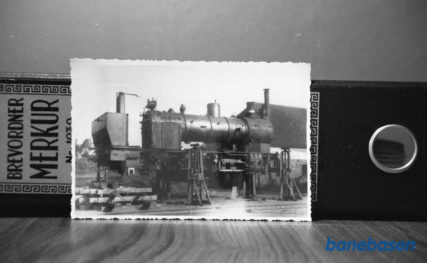 Det "afklædte" lokomotiv er et af Gudhjembanens to lokomotiver, som renoveres på Gudhjem station, formentlig i 1928. På daværende tidspunkt lå Nexø-banen endnu med det oprindelige spor, som var for spinkelt til at kunne bære disse lokomotiver Det "afklædte" lokomotiv er et af Gudhjembanens to lokomotiver, som renoveres på Gudhjem station, formentlig i 1928. På daværende tidspunkt lå Nexø-banen endnu med det oprindelige spor, som var for spinkelt til at kunne bære disse lokomotiver