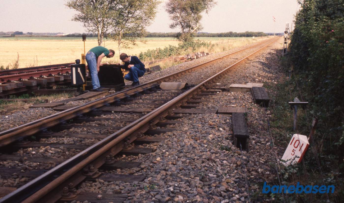2 personer inspicerer den mekaniske aflåsning af et sporskifte. Det ene sæt wire i højre side går til at skifte sporskiftet, mens det andet sæt går til at aflåse sporskiftet mod utidig omstilling 2 personer inspicerer den mekaniske aflåsning af et sporskifte. Det ene sæt wire i højre side går til at skifte sporskiftet, mens det andet sæt går til at aflåse sporskiftet mod utidig omstilling