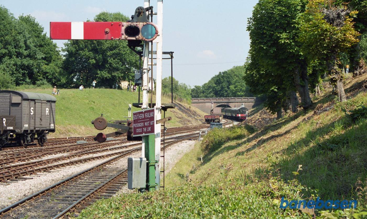 Et armsignal i forgrunden og et persontog ude under viadukten, på vej ind på stationen