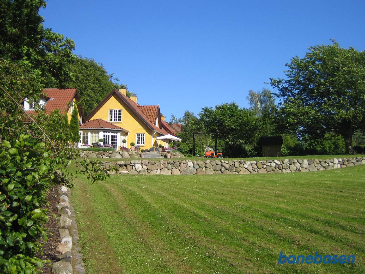 Det gule hus på den anden side af hækken. Ravnsholt skov til venstre. Banen gik i sin tid henover græsplænen Det gule hus på den anden side af hækken. Ravnsholt skov til venstre. Banen gik i sin tid henover græsplænen