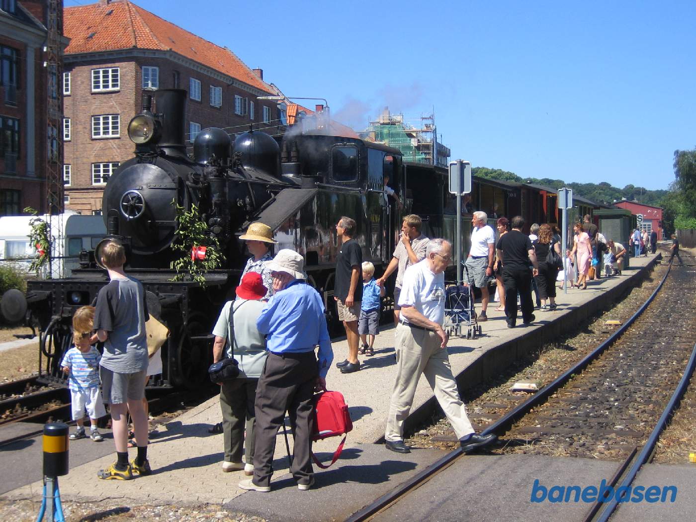 Damptoget ankommet til Grønnehave, hvor passagererne stiger ud og kigger på det fint pyntede damplokomotiv