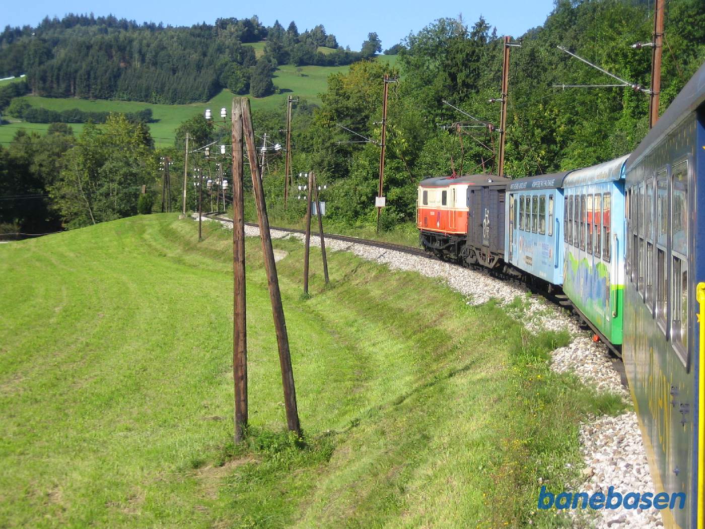 Toget kører i et bakket landskab med græsmarker til venstre og skov til højre