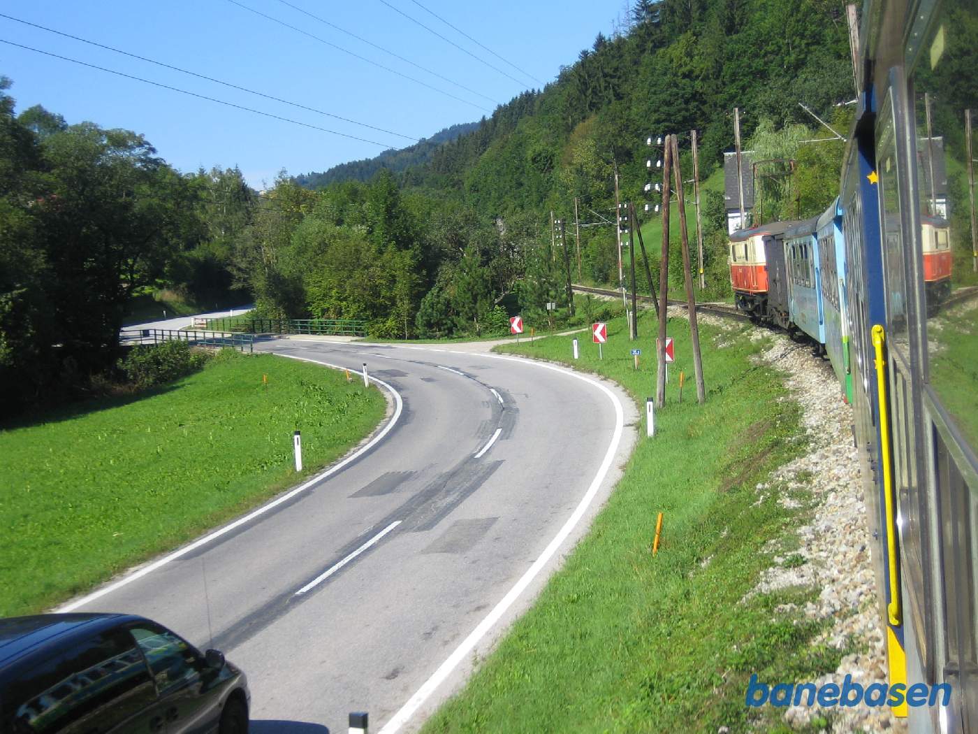 Toget kører i et kuperet landskab, vejen og floden til venstre