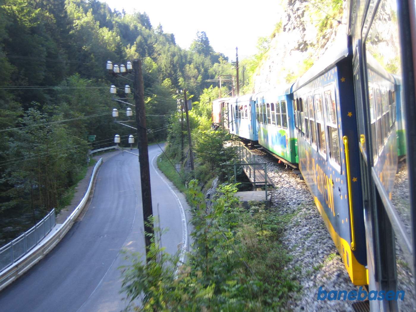 Toget kører i et kuperet landskab, vejen og floden til venstre