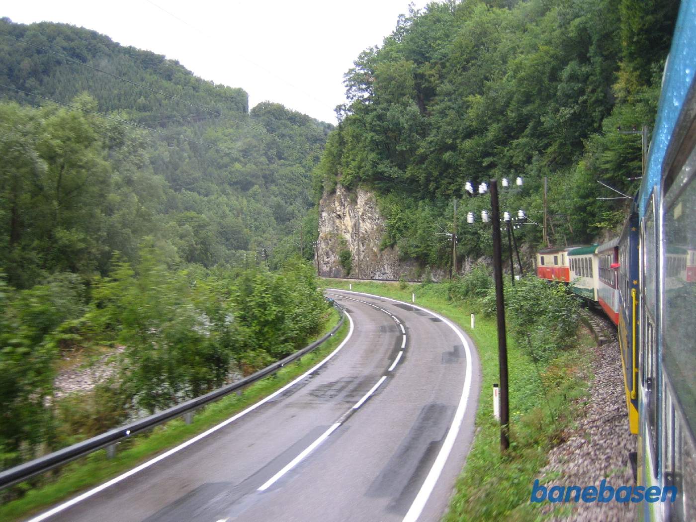 Toget kører langs vejen og floden til venstre i det kuperede landskab