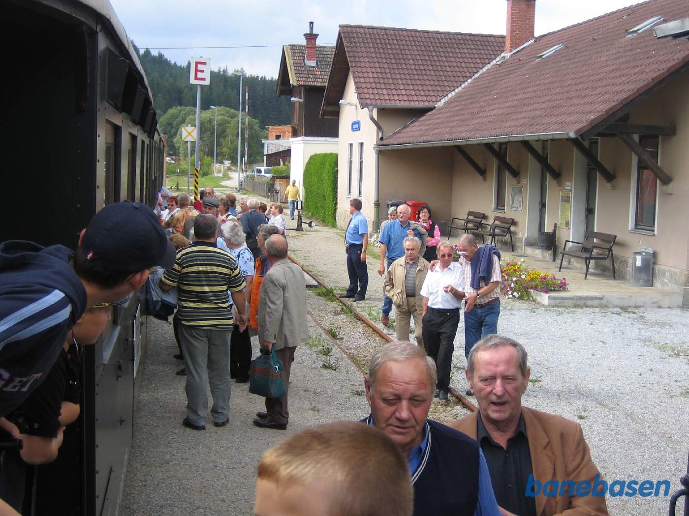 Persontoget ved perron, mange rejsende myldrer ind i toget, stationsbygningen til højre