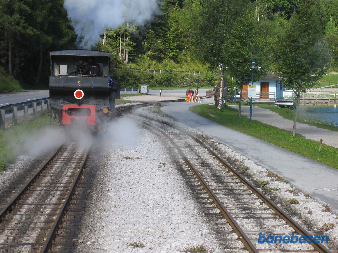 Damplokomotivet løber om vognen. Midt i billedet ses stopbommen af en blomsterkasse. Skibsbroen i højre side af billedet
