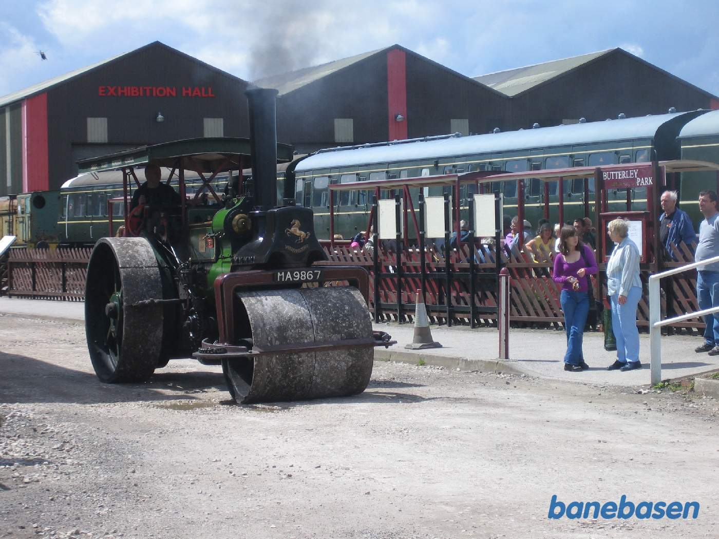 En damptromle kører forbi smalsporsstationen