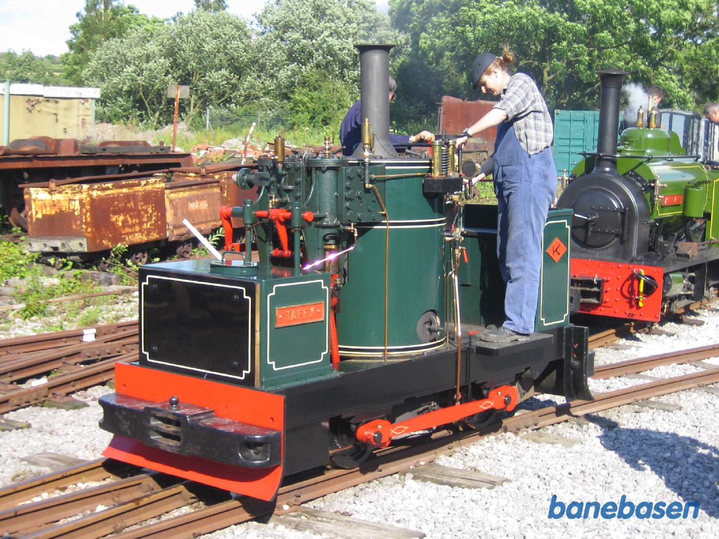 Det lille damplokomotiv kører i sporet ind til remisen, mens det grønne lokomotiv holder i hovedsporet