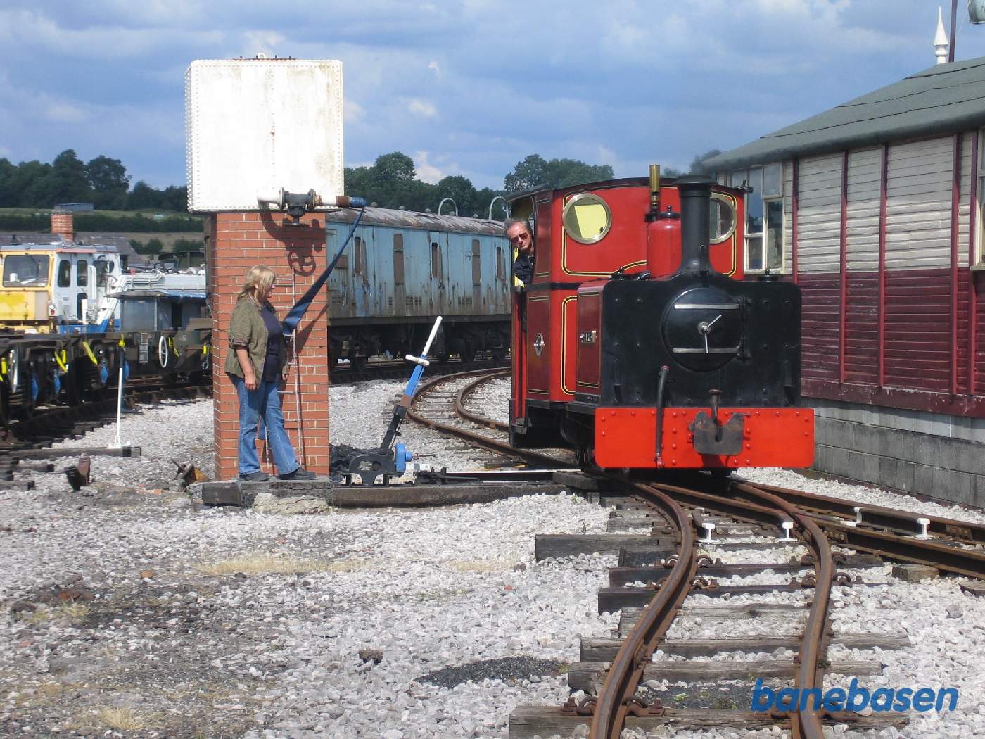 Det røde lokomotiv passerer stationsbygningen til GVLR. Maskinchefens kone står klar med vandslangen
