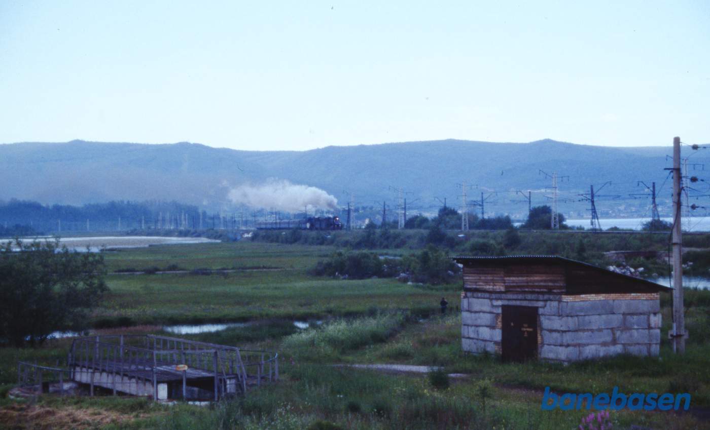 Et udflugtstog med 2 damplokomotiver havde været på tur til Port Baikal og er nu på vej tilbage til Sludyanka en sen eftermiddag. Baikalsøen ses på den anden side af jernbanen