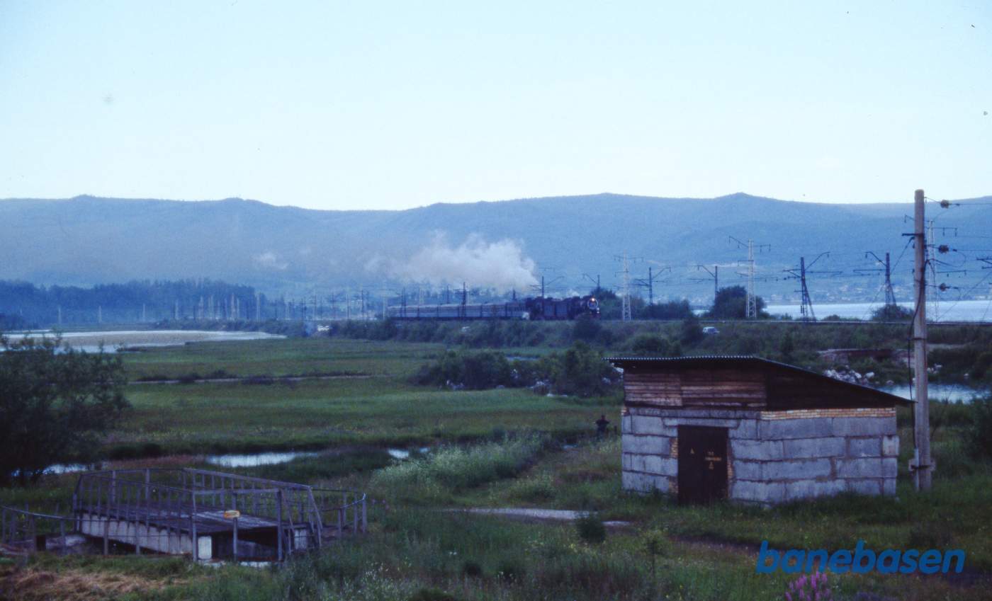 Et udflugtstog med 2 damplokomotiver havde været på tur til Port Baikal og er nu på vej tilbage til Sludyanka en sen eftermiddag. Baikalsøen ses på den anden side af jernbanen
