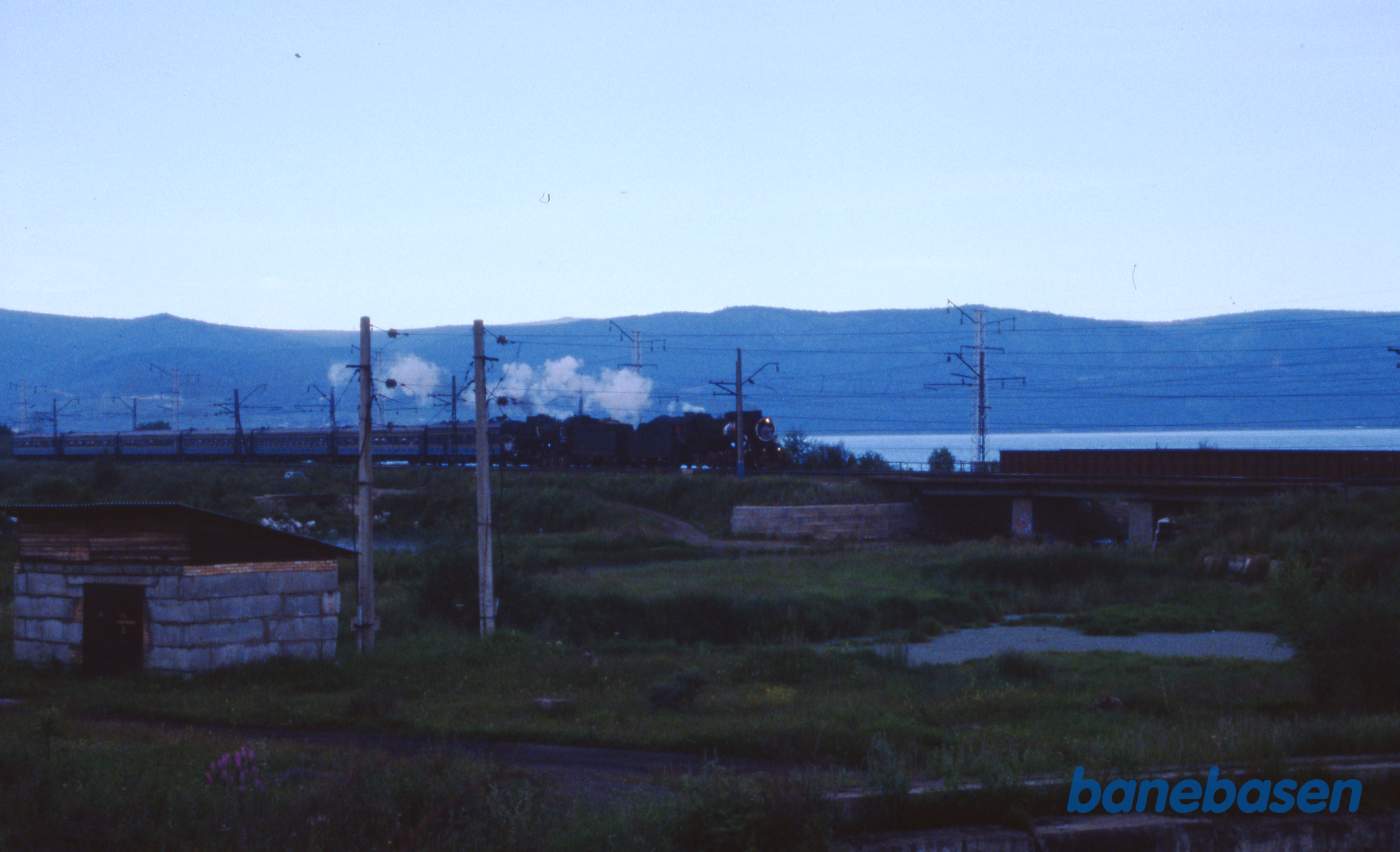 Et udflugtstog med 2 damplokomotiver havde været på tur til Port Baikal og er nu på vej tilbage til Sludyanka en sen eftermiddag. Baikalsøen ses på den anden side af jernbanen