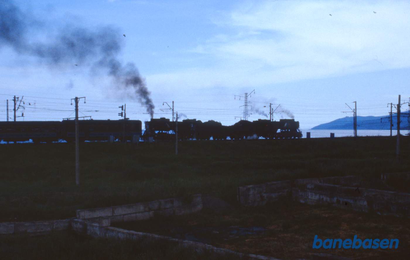 Et udflugtstog med 2 damplokomotiver havde været på tur til Port Baikal og er nu på vej tilbage til Sludyanka en sen eftermiddag. Baikalsøen ses på den anden side af jernbanen