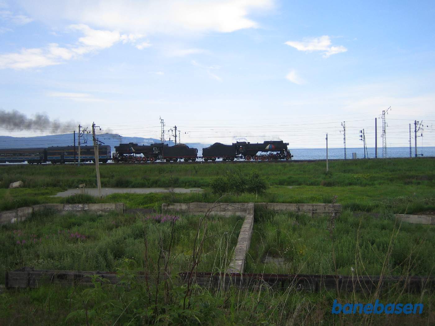 Et turisttog med 2 damplokomotiver fra Port Baikal på vej ind mod Sludyanka station, Baikal søen bag toget