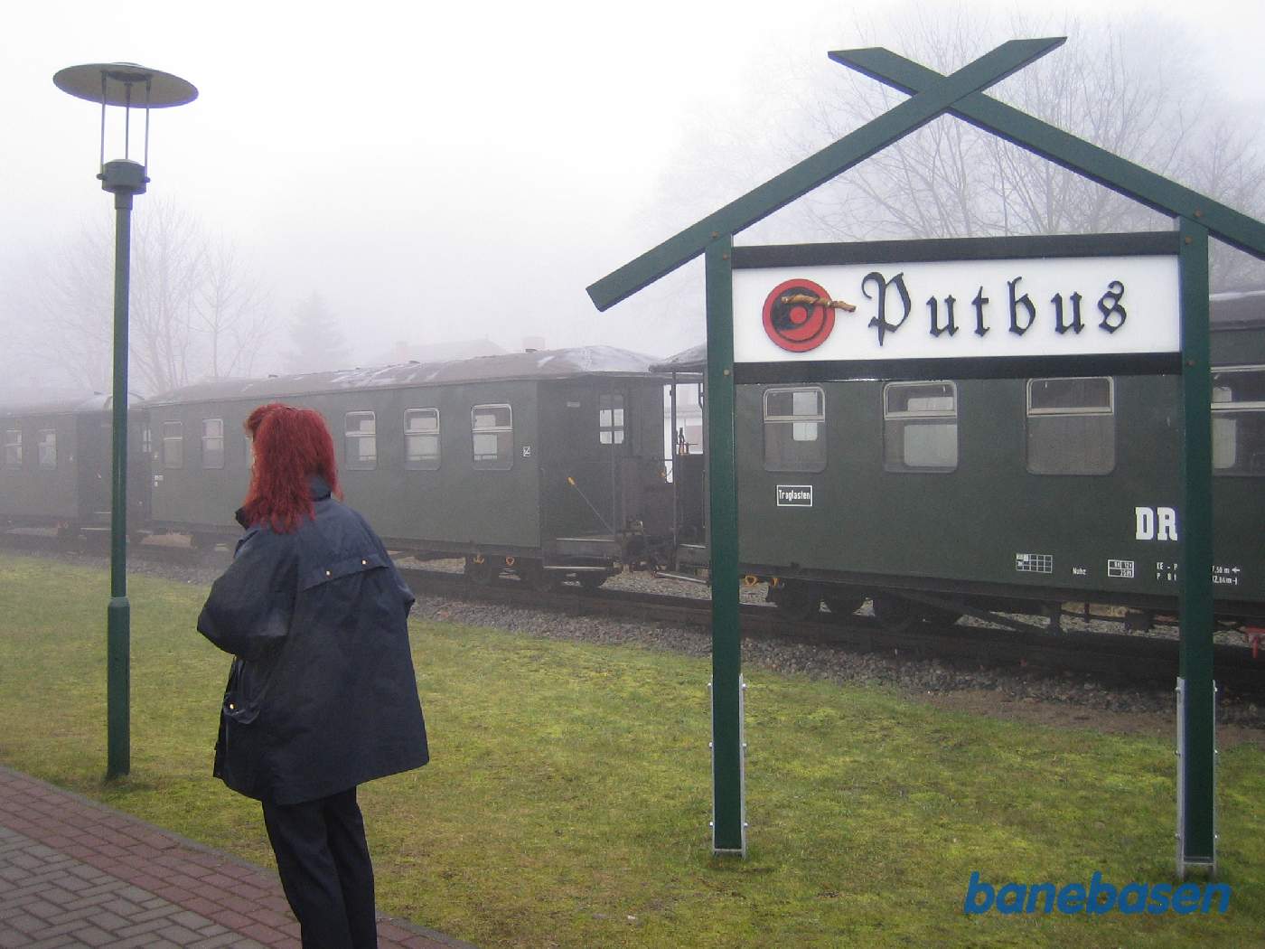 Stationsskilt på perronen, togføreren står med ryggen til