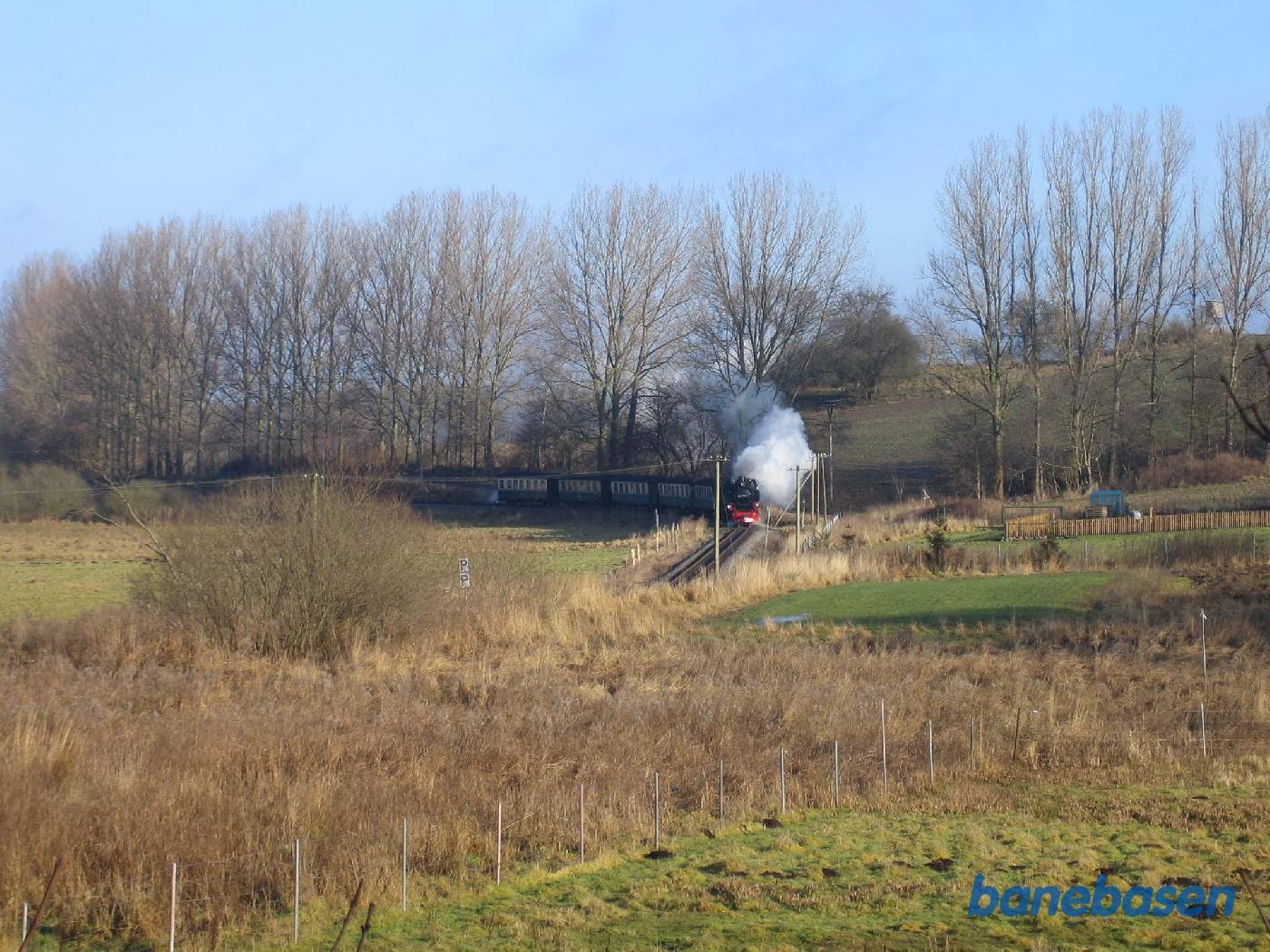 Et damptog kommer kørende rundt i en kurve lige før trinbrættet, set fra en bakke