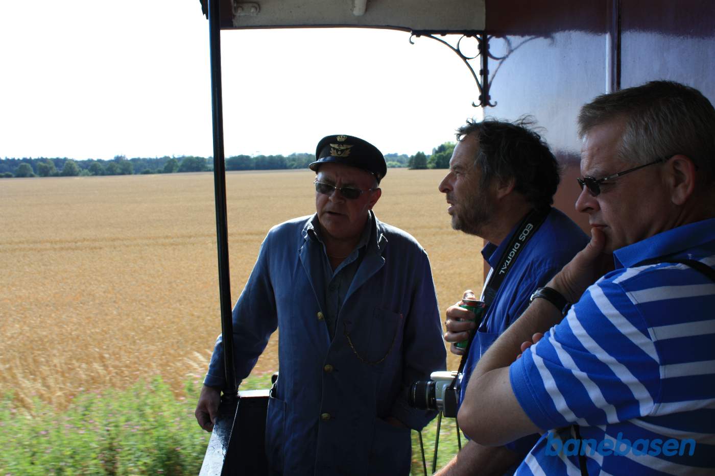 2 turister får en jernbanesnak med rangerlederen ude på en åben endeperron lige efter lokomotivet