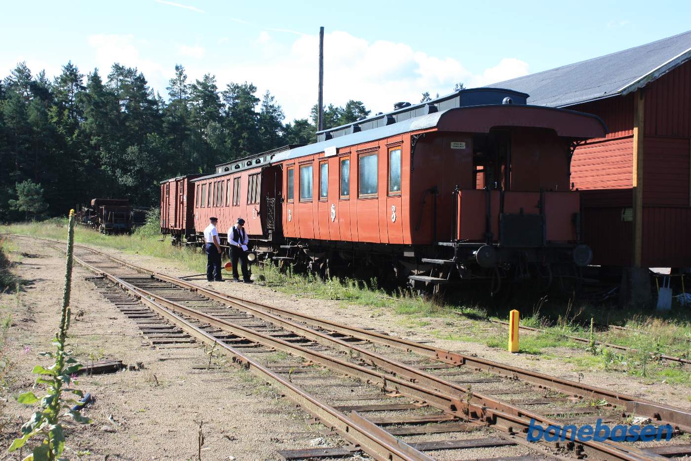To klubmedlemmer står foran nogle fine gamle tagryttervogne