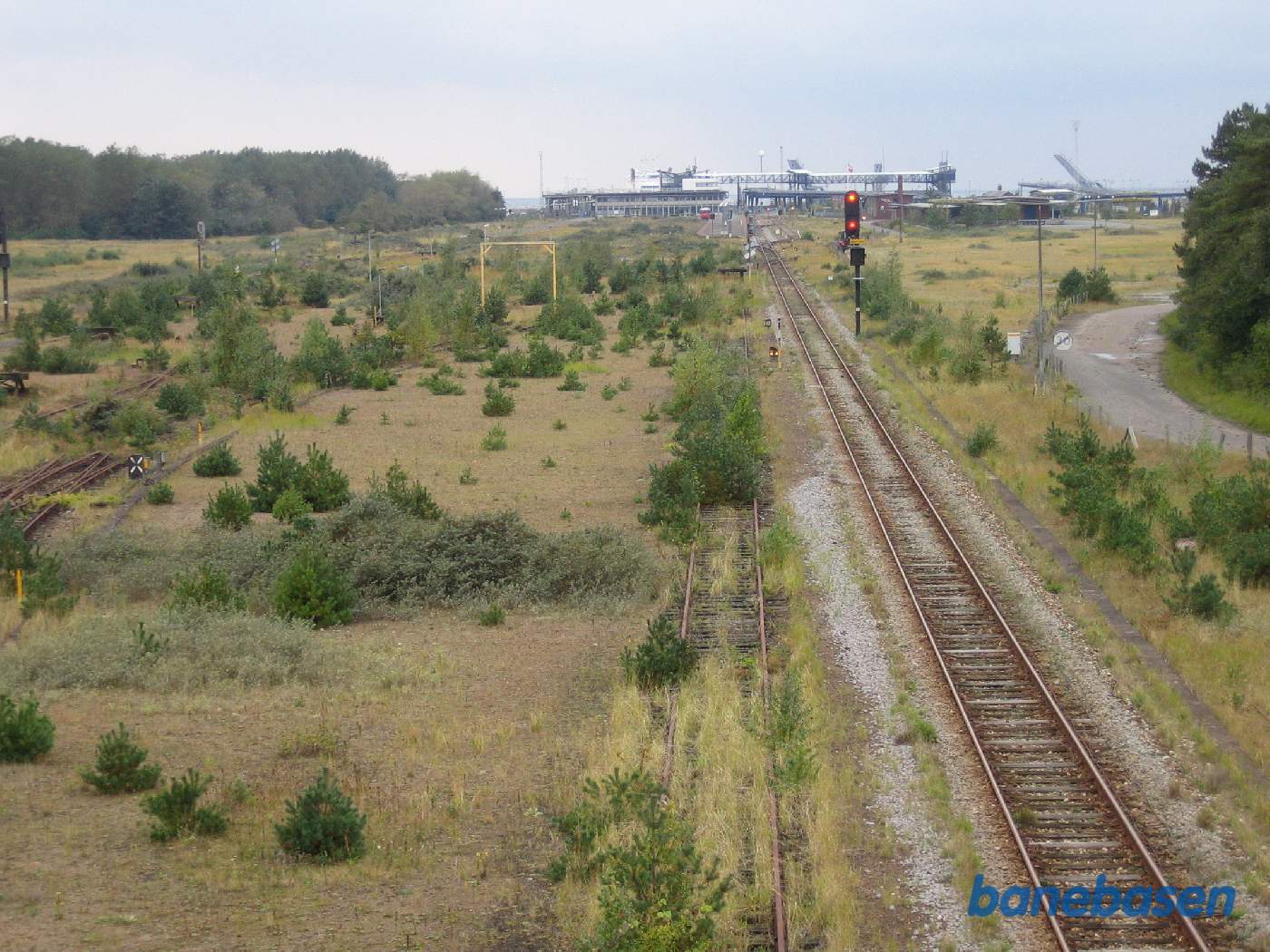 Et vue fra vejbroen ned over baneområdet. Hovedsporet med I-signalet går til Rødby Færge personbanegård. Godsbanegården er de mange overgroede spor til venstre Et vue fra vejbroen ned over baneområdet. Hovedsporet med I-signalet går til Rødby Færge personbanegård. Godsbanegården er de mange overgroede spor til venstre