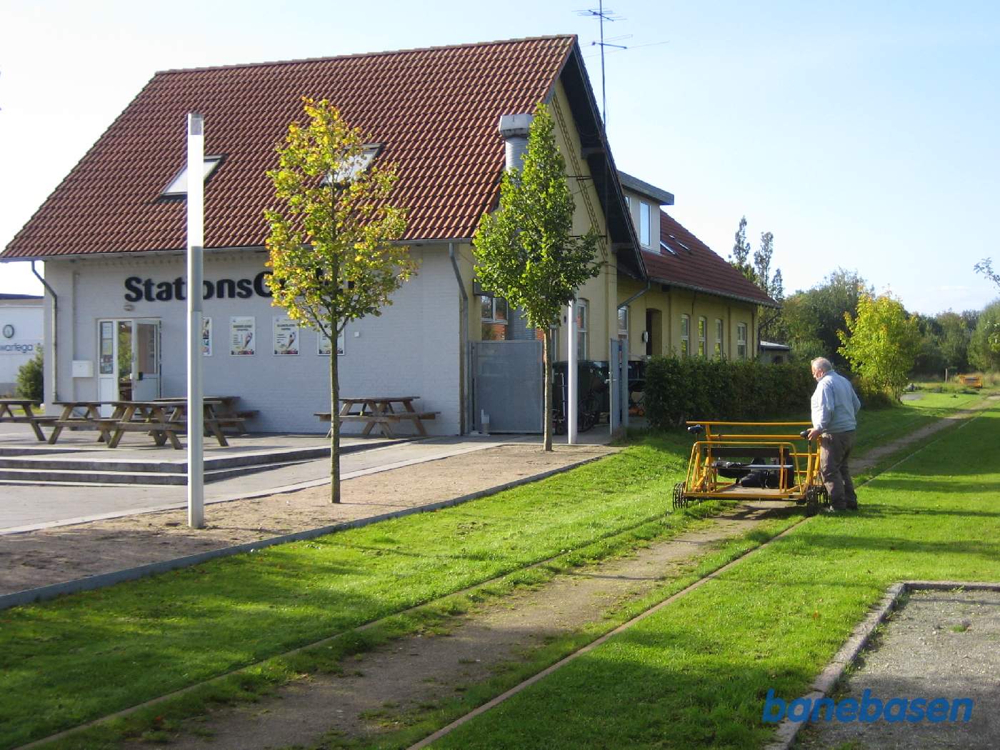Cyklisten holder en velfortjent pause. Stationsbygningen ses inde til venstre