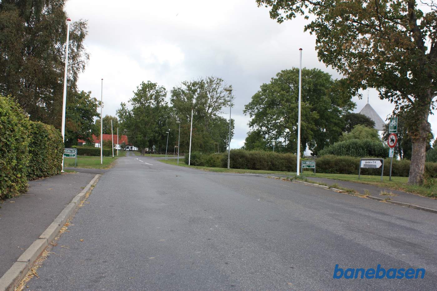 Vi står på Kirkevej og kigger op mod kirken. De grønne skilte viser, hvor banen krydsede vejen