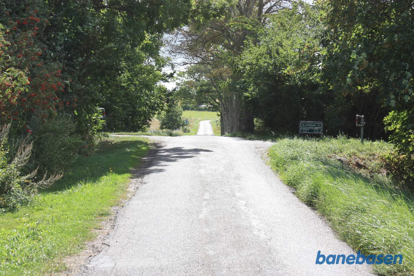 Vi står på en anden overkørsel ved Fejleregårdsvejen, hvor det tydeligt ses, at vejen går op til banens tracé på begge sider, Aakirkeby til venstre og Rønne til højre