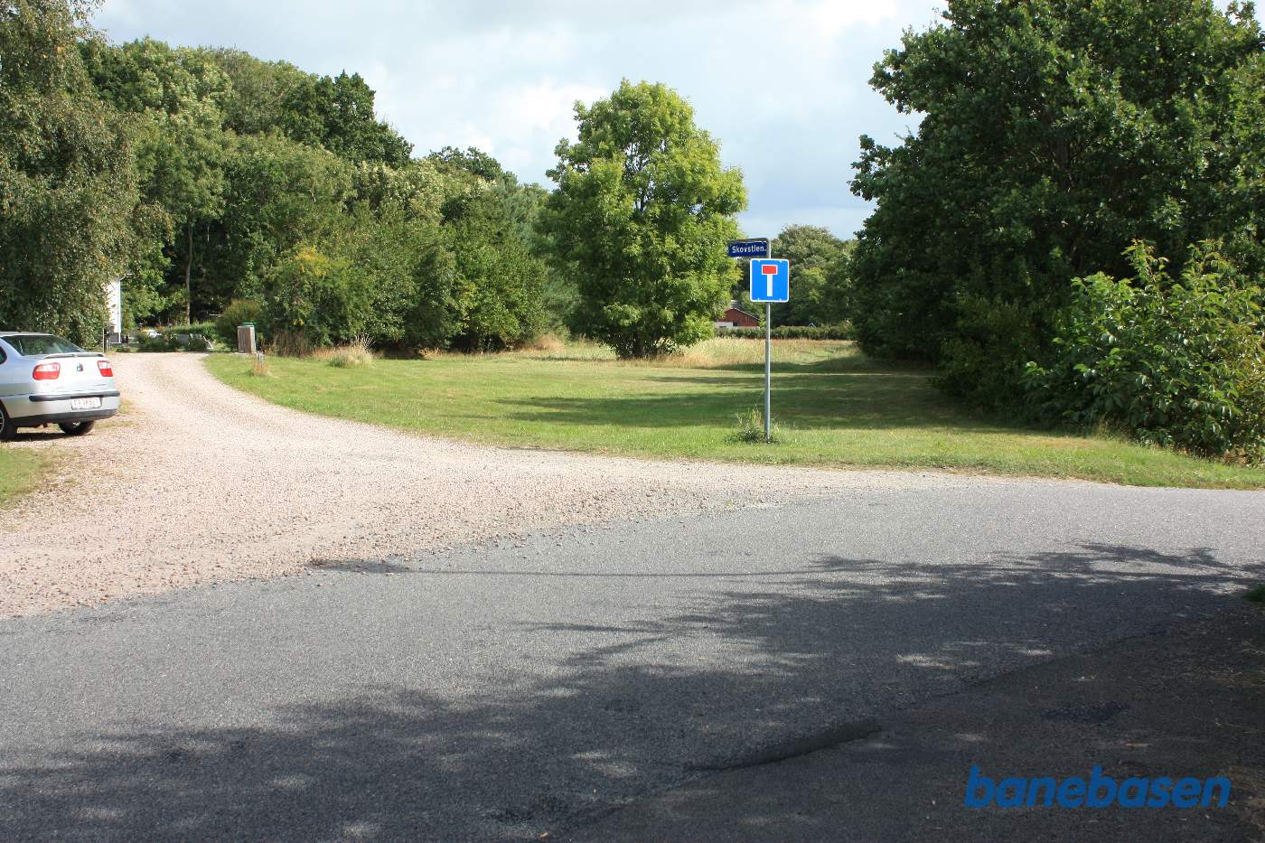Vi står på Jernbanevej og kigger i retning mod Nexø. Foran os har vi hele sporarealet foran stationen. Stationsbygningen gemmer sig bag træerne til højre