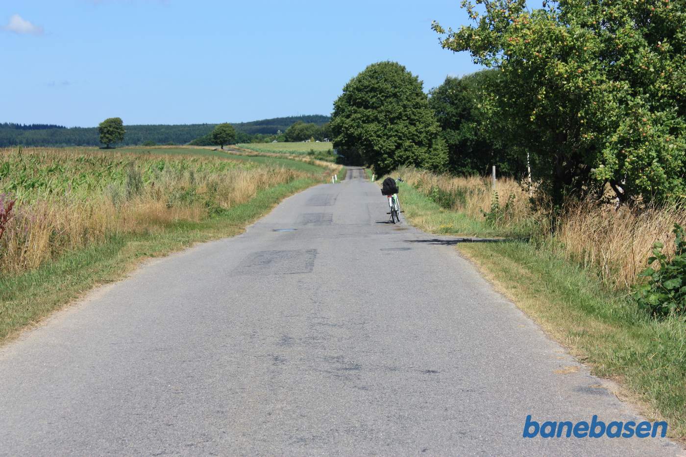 Vi står på Smørengevejen og kigger mod nord. Cyklen er parkeret præcist der hvor banen krydsede vejen, Rønne til venstre og Nexø til højre. Smørenge lå lige venstre for vejen