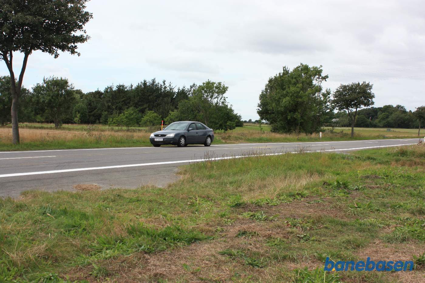Vi er på Grammegårdsvej og bilen markerer hvor banen krydsede vejen, vi kigger i retning mod Rønne Vi er på Grammegårdsvej og bilen markerer hvor banen krydsede vejen, vi kigger i retning mod Rønne