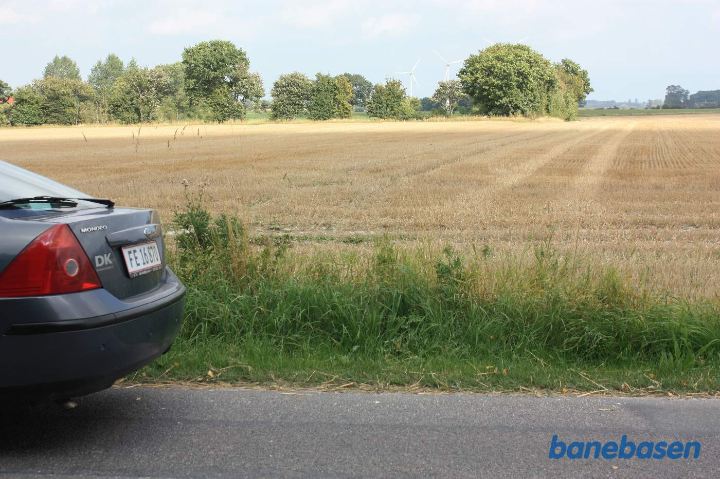 Vi er på Brandsgårdsvejen og kigger mod Nexø. Banen gik i en stor bue over mod træerne til højre for de 2 hvide vindmøller, der står på den gamle banetracé Vi er på Brandsgårdsvejen og kigger mod Nexø. Banen gik i en stor bue over mod træerne til højre for de 2 hvide vindmøller, der står på den gamle banetracé