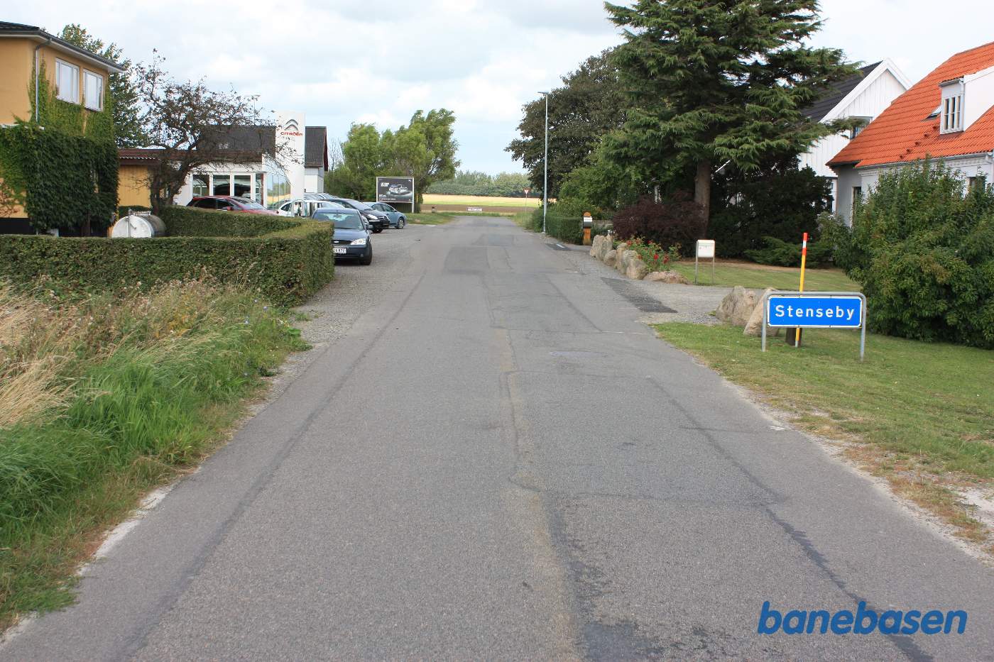 Vi står på Vangsbovej og kigger op mod stationen der skimtes som det sidste hus i vejens venstre side. Banen krydsede over vejen ved det store skilt til venstre Vi står på Vangsbovej og kigger op mod stationen der skimtes som det sidste hus i vejens venstre side. Banen krydsede over vejen ved det store skilt til venstre