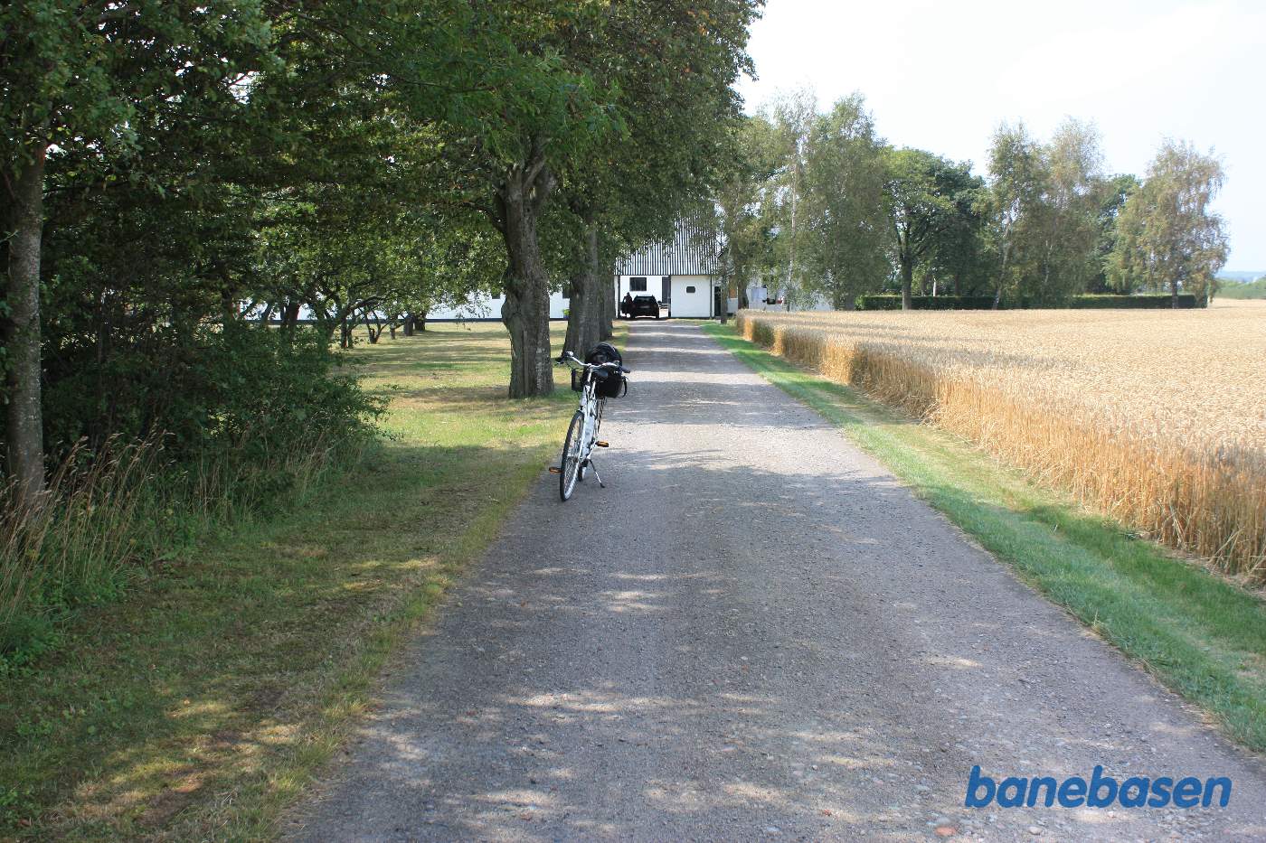 Vi står på alléen op til gården. Cyklen markerer hvor banen krydsede vejen. Rønne til venstre og Sandvig til højre Vi står på alléen op til gården. Cyklen markerer hvor banen krydsede vejen. Rønne til venstre og Sandvig til højre