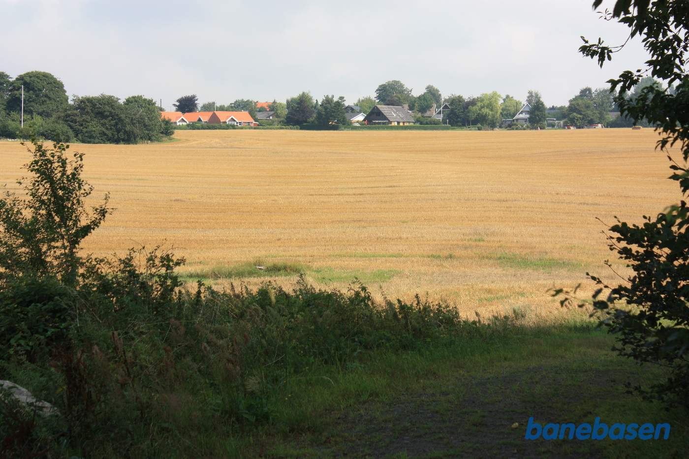 Vi står ved Aagaardsvej og kigger mod Sandvig. Banen gik på en høj banedæmning over markerne i en blød bue højre om træerne til venstre og ind i Klemensker til venstre for typehusene med rødt tag Vi står ved Aagaardsvej og kigger mod Sandvig. Banen gik på en høj banedæmning over markerne i en blød bue højre om træerne til venstre og ind i Klemensker til venstre for typehusene med rødt tag