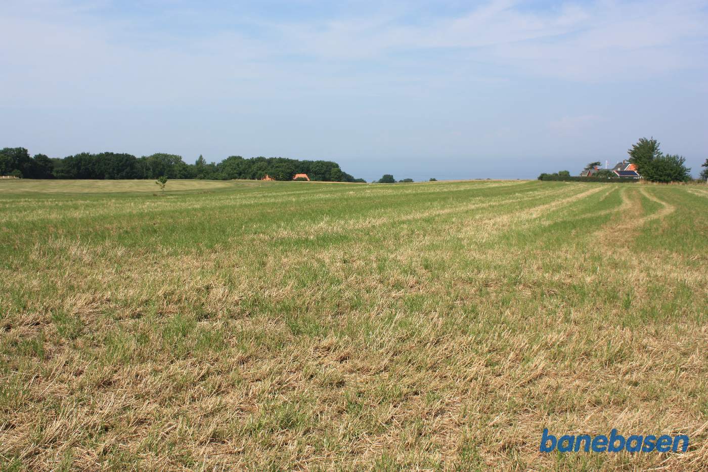 Vi er lige udenfor byen og kigger i retning mod Sandvig. Banen gik i en stor blød venstrebue ud over marken, foran gården med rødt tag, og ind i skoven til venstre
