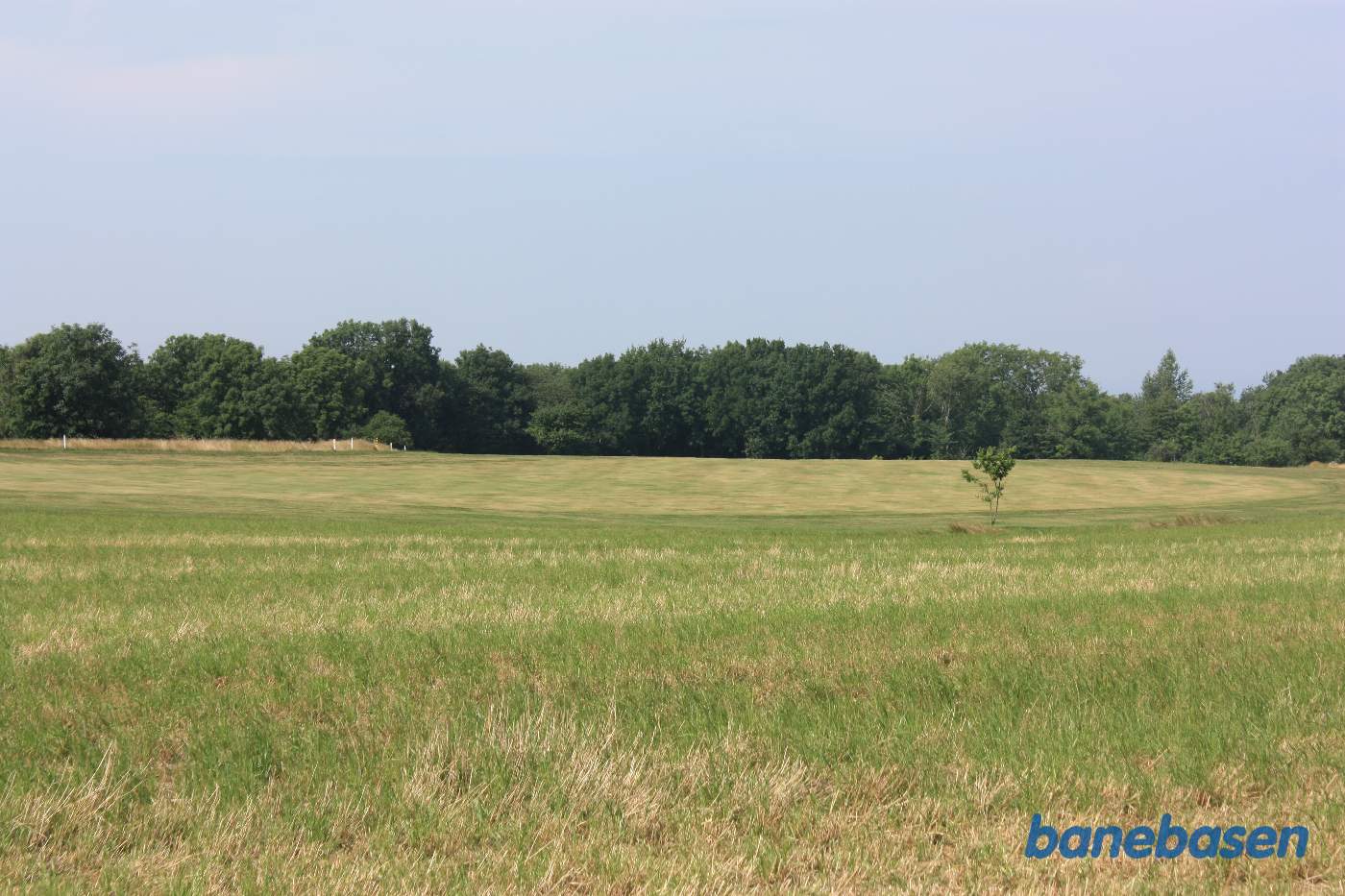 Vi er lige udenfor byen og kigger i retning mod Sandvig. Banen gik i en stor blød venstrebue ud over marken og ind i skoven midt for Vi er lige udenfor byen og kigger i retning mod Sandvig. Banen gik i en stor blød venstrebue ud over marken og ind i skoven midt for