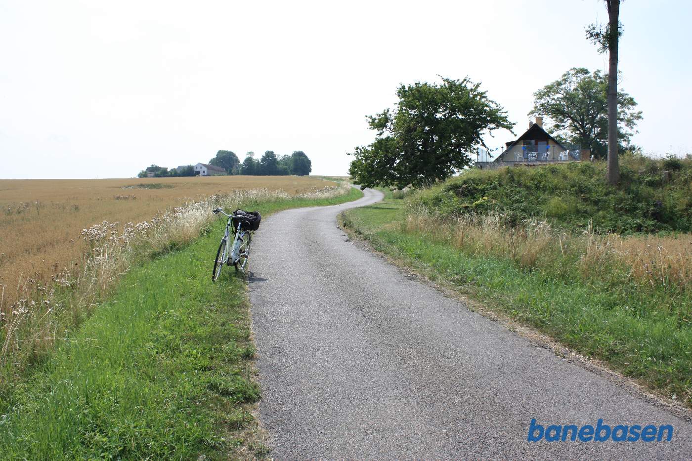 Vi står på Dynddalsvej hvor banen krydsede over vejen. Der er stadig raster af den høje banedæmning til højre foran huset. Rønne til venstre og Sandvig til højre Vi står på Dynddalsvej hvor banen krydsede over vejen. Der er stadig raster af den høje banedæmning til højre foran huset. Rønne til venstre og Sandvig til højre