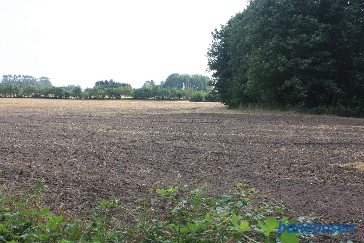 Vi står ude på marken og kigger ind mod Aakirkeby. Banen gik i en blød højre bue rundt om træerne lige fremme og højre om de store træer ude i horisonten