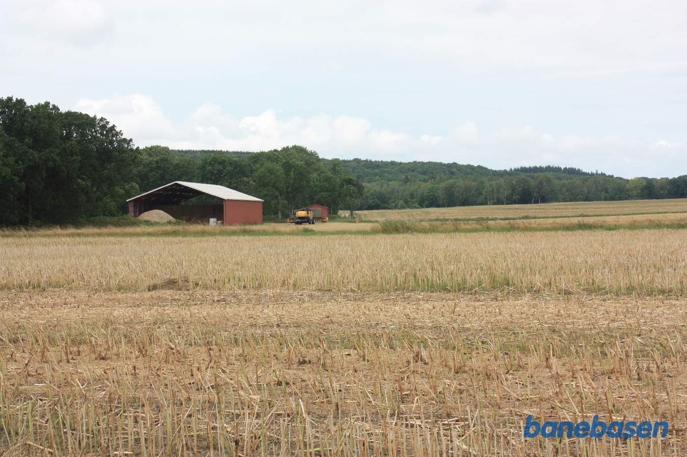 Vi står i et markskel og kigger mod Gudhjem. Banen gik midt i billedet og fortsatte ad de to hjulspor der ses efter laden