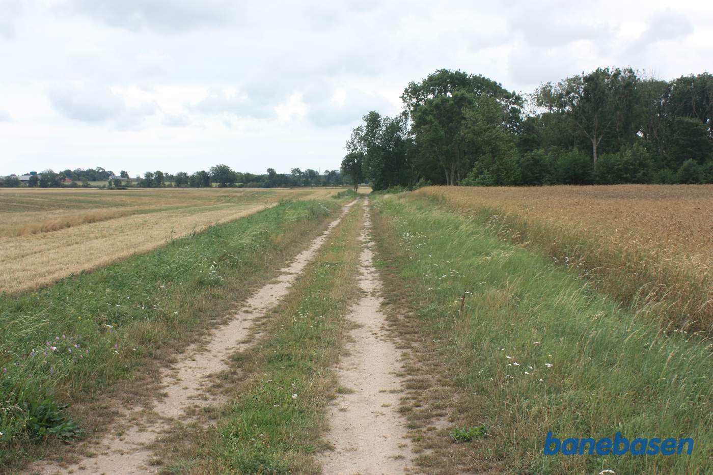 Vi står på den gamle banetracé og kigger mod Aakirkeby. Vallensgaard trinbræt lå nede ved træerne Vi står på den gamle banetracé og kigger mod Aakirkeby. Vallensgaard trinbræt lå nede ved træerne