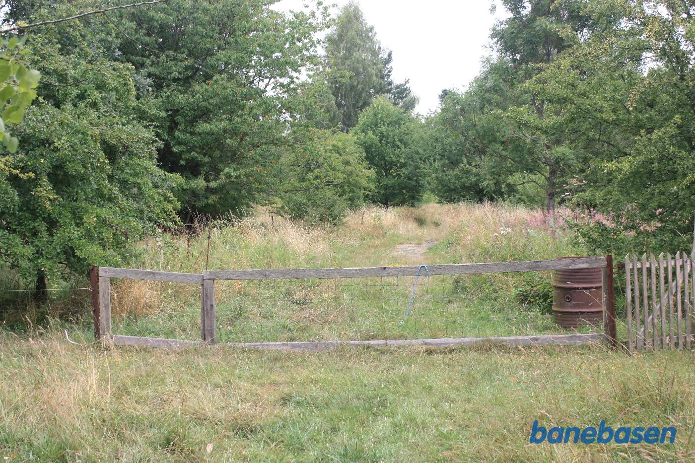 Vi står på den gamle banetracé og kigger mod Gudhjem. Her forgrenede banen sig mod den gamle stationsbygning til venstre og mod Gudhjem til højre Vi står på den gamle banetracé og kigger mod Gudhjem. Her forgrenede banen sig mod den gamle stationsbygning til venstre og mod Gudhjem til højre