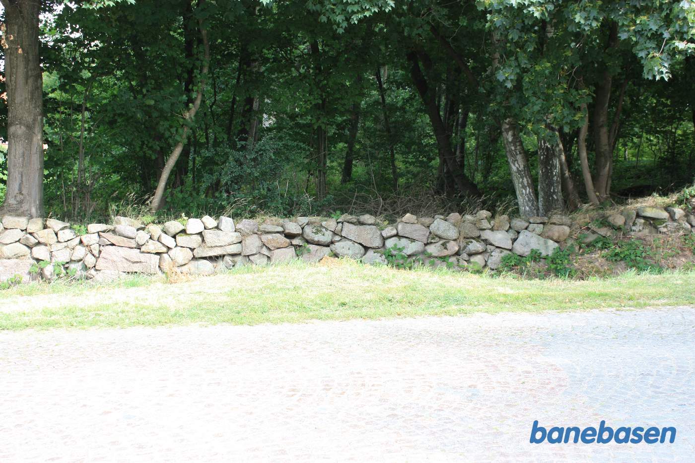 Vi står på Ekkodalsvejen og kigger mod Gudhjem, hvor banen gik gennem skoven og forbi den store gård Rømersdal til venstre for banen Vi står på Ekkodalsvejen og kigger mod Gudhjem, hvor banen gik gennem skoven og forbi den store gård Rømersdal til venstre for banen