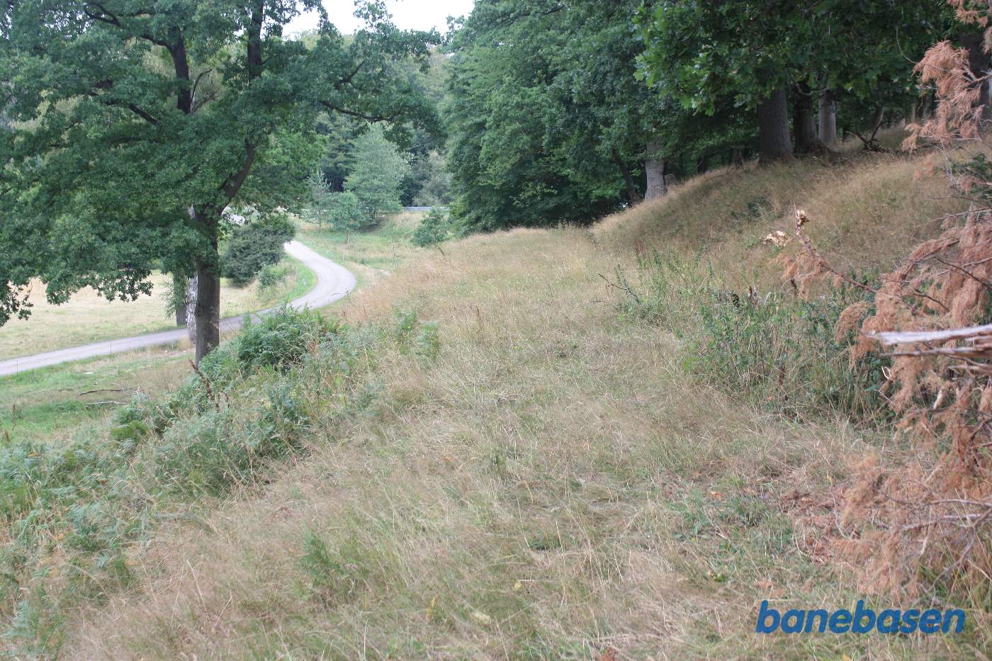 Vi står på den gamle banetracé og kigger mod Gudhjem. Banen slog en kurve mod venstre - man kan følge banedæmningen. Almindingsvejen ses længere fremme Vi står på den gamle banetracé og kigger mod Gudhjem. Banen slog en kurve mod venstre - man kan følge banedæmningen. Almindingsvejen ses længere fremme